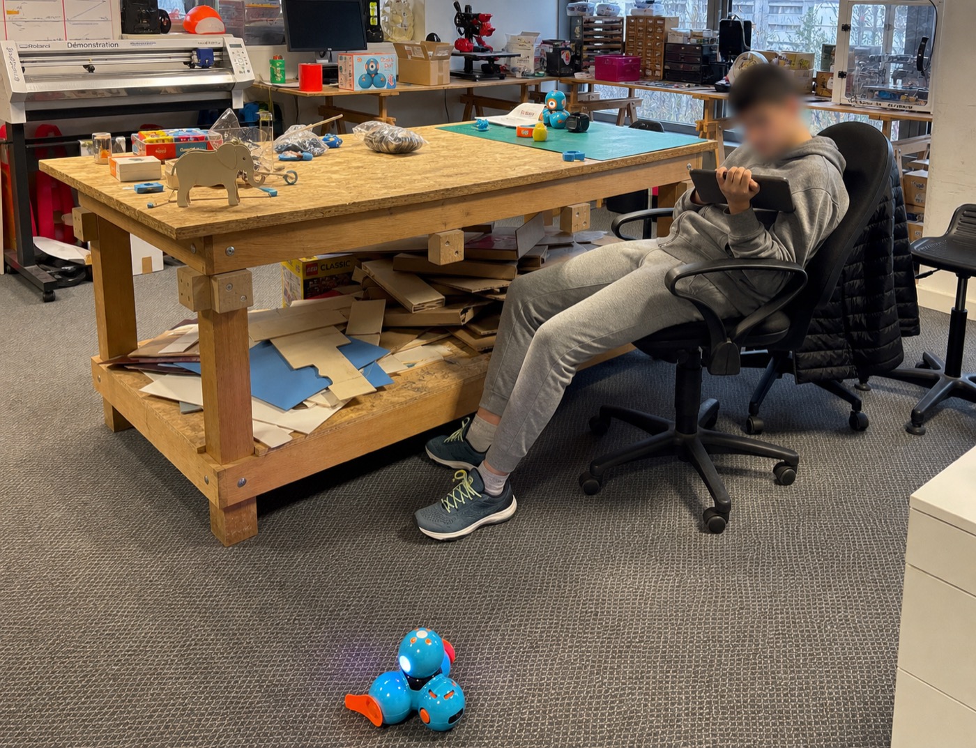 Accompagnement numérique individuel avec tablette et robot dans un atelier, visage flouté.